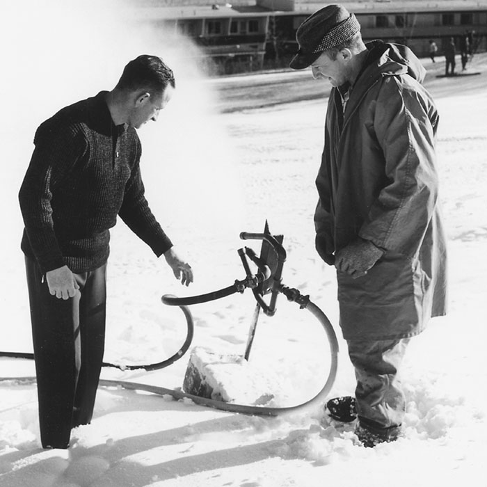 A black and white image showing two men inspecting a snowmaking gun.